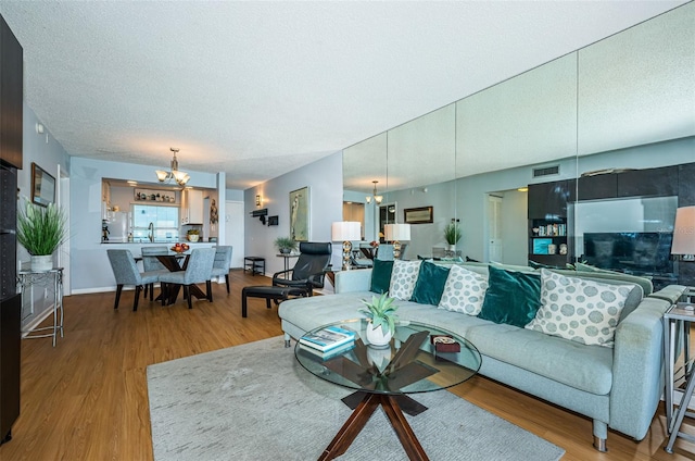 living room featuring a chandelier, a textured ceiling, wood finished floors, and visible vents