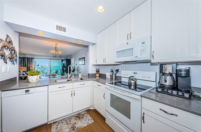 kitchen with white appliances, visible vents, white cabinets, wood finished floors, and a sink