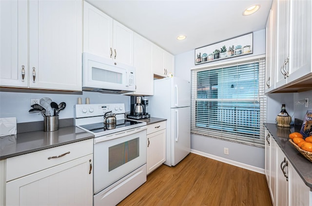 kitchen with dark countertops, white appliances, light wood-type flooring, and white cabinets