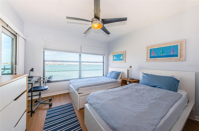 bedroom with a water view, multiple windows, a ceiling fan, and wood finished floors