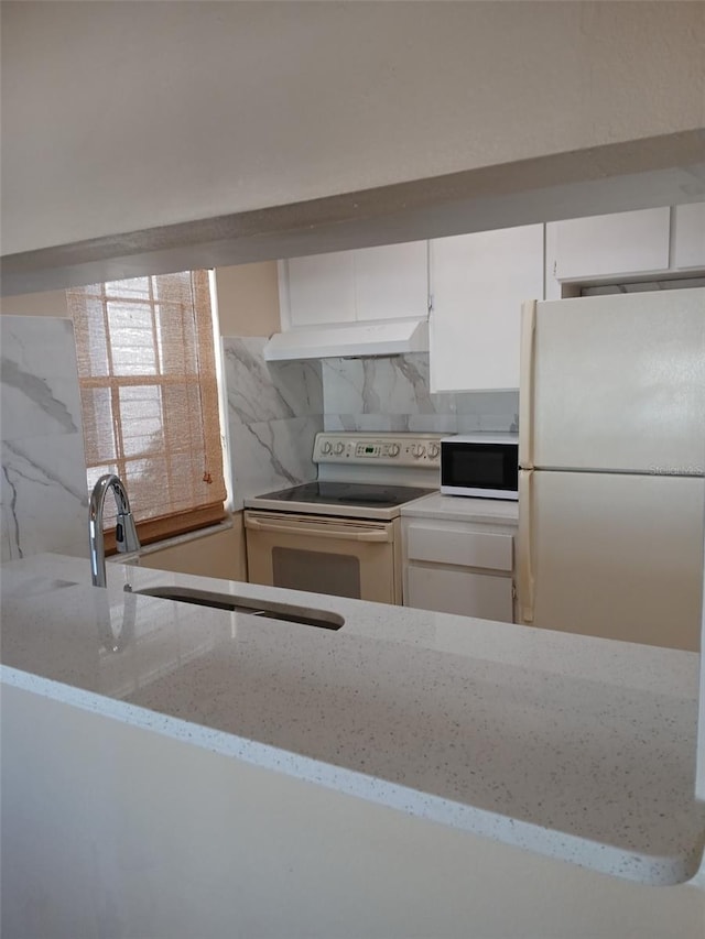 kitchen with white appliances, white cabinets, light stone counters, under cabinet range hood, and backsplash