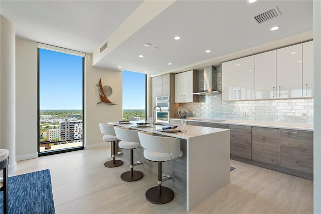 kitchen with wall chimney range hood, modern cabinets, and visible vents