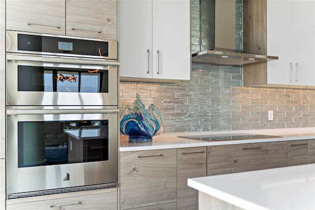 kitchen with double oven, backsplash, wall chimney range hood, and modern cabinets