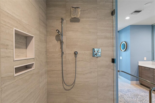 bathroom featuring tiled shower, vanity, visible vents, and baseboards