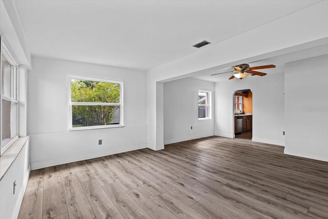 empty room featuring arched walkways, wood finished floors, a ceiling fan, visible vents, and baseboards