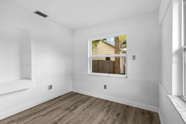 spare room with wood finished floors, visible vents, and baseboards