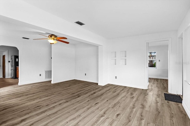 unfurnished living room with arched walkways, visible vents, a ceiling fan, wood finished floors, and baseboards