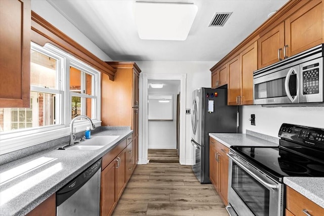 kitchen with visible vents, appliances with stainless steel finishes, brown cabinetry, a sink, and light wood-type flooring