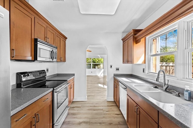 kitchen featuring arched walkways, a sink, appliances with stainless steel finishes, light wood-type flooring, and brown cabinets