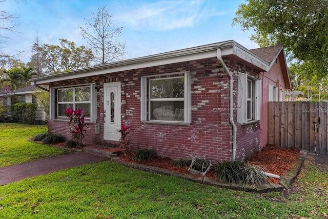 bungalow-style home with a front lawn, fence, and brick siding