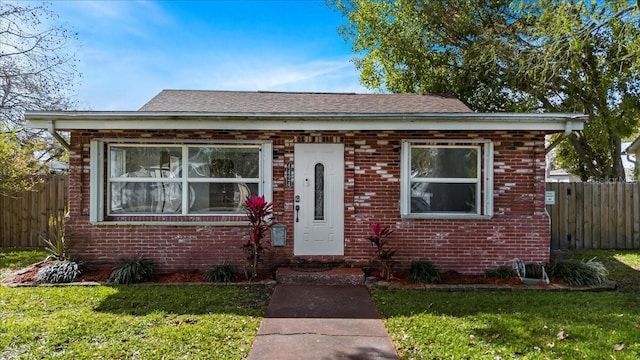 bungalow-style house with brick siding, roof with shingles, a front lawn, and fence