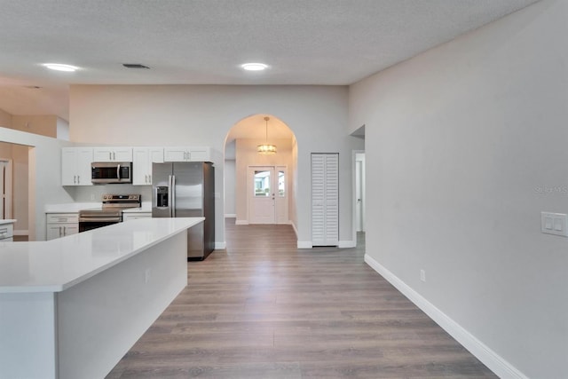 kitchen featuring arched walkways, appliances with stainless steel finishes, wood finished floors, light countertops, and white cabinetry