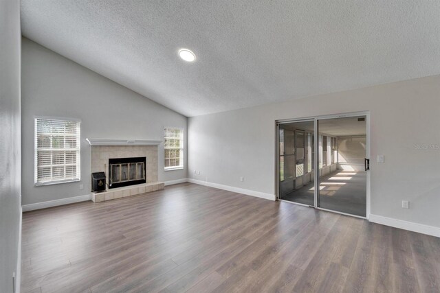 unfurnished living room with lofted ceiling, baseboards, a tiled fireplace, and wood finished floors