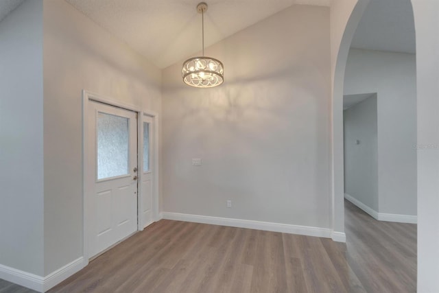 entrance foyer featuring baseboards, arched walkways, wood finished floors, an inviting chandelier, and vaulted ceiling