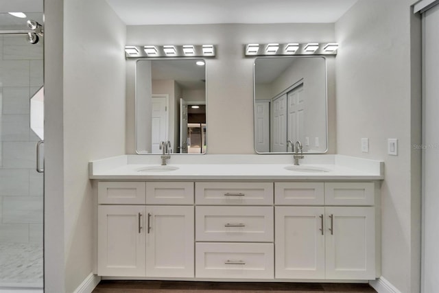 bathroom with double vanity, a stall shower, a sink, and baseboards