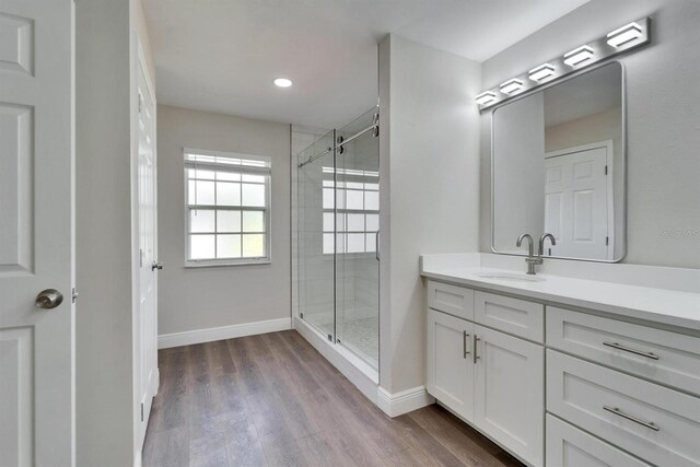 bathroom with baseboards, wood finished floors, vanity, a shower stall, and recessed lighting