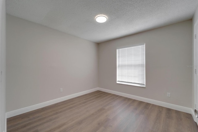 unfurnished room with a textured ceiling, wood finished floors, and baseboards