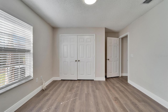 unfurnished bedroom with a closet, visible vents, a textured ceiling, wood finished floors, and baseboards