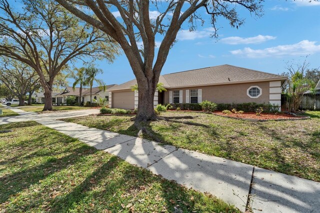 view of front of home with driveway, an attached garage, a front lawn, and stucco siding