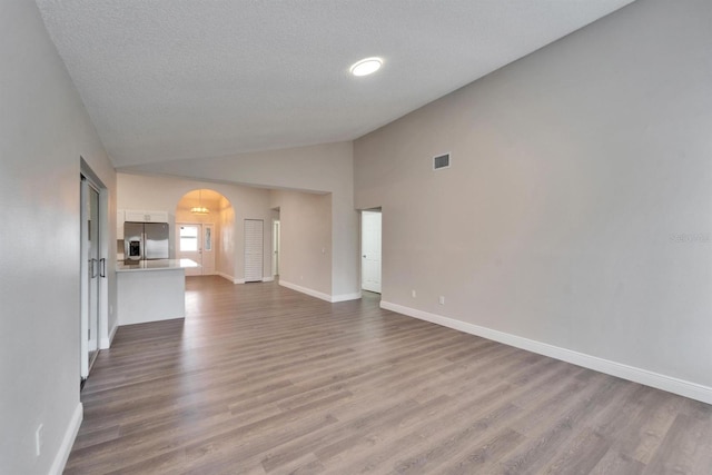 unfurnished living room featuring baseboards, arched walkways, visible vents, dark wood finished floors, and vaulted ceiling