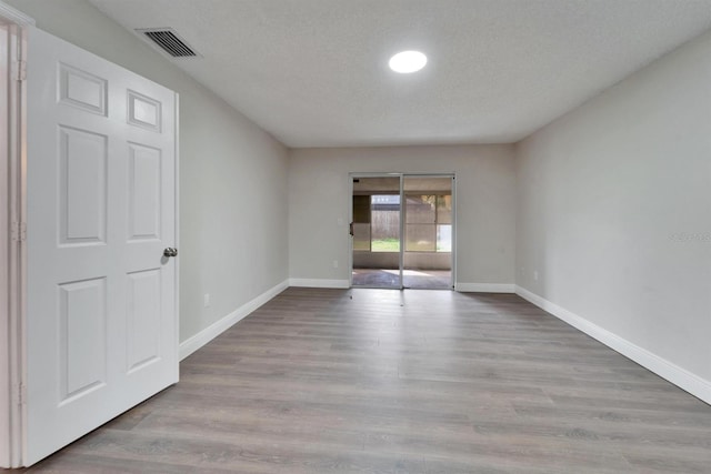 spare room featuring baseboards, a textured ceiling, visible vents, and wood finished floors