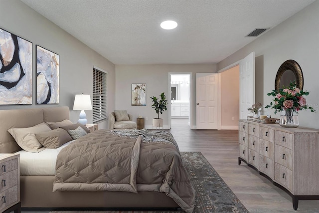 bedroom with a textured ceiling, connected bathroom, wood finished floors, visible vents, and baseboards