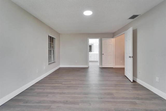 unfurnished room with visible vents, a textured ceiling, baseboards, and wood finished floors