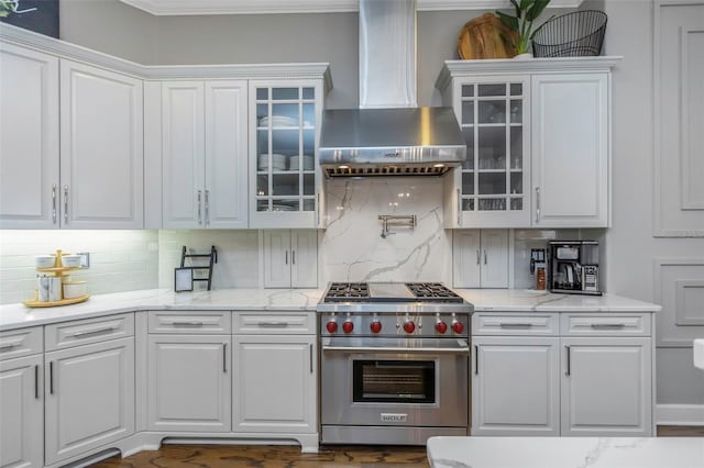 kitchen with tasteful backsplash, white cabinetry, premium stove, and wall chimney exhaust hood