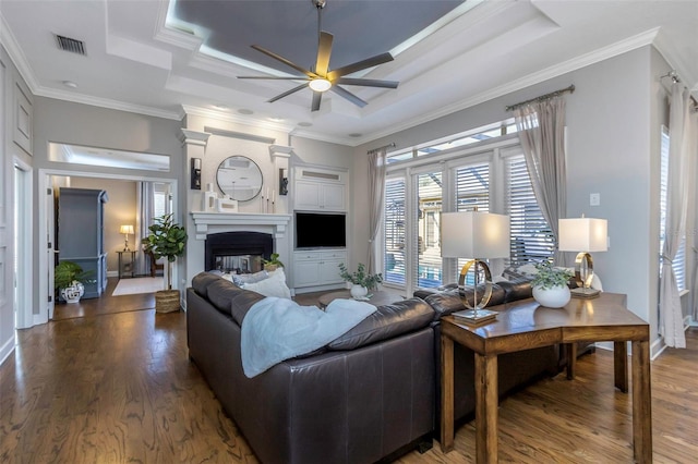 living room with wood finished floors, a glass covered fireplace, a raised ceiling, and visible vents