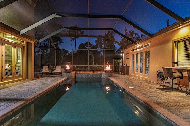 pool at night featuring a lanai, a pool with connected hot tub, a patio, and french doors