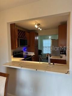 kitchen featuring a peninsula, brown cabinets, light countertops, and stainless steel range with electric cooktop