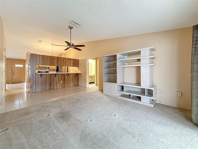 unfurnished living room with light colored carpet, visible vents, a ceiling fan, light tile patterned flooring, and a textured ceiling