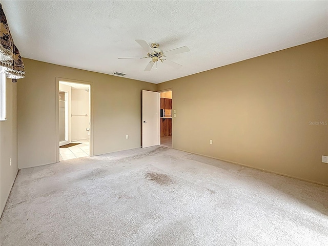 spare room with a ceiling fan, light colored carpet, visible vents, and a textured ceiling