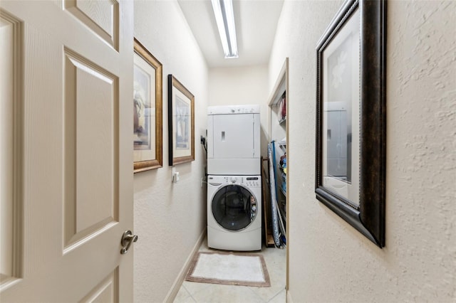 laundry area with a textured wall, laundry area, stacked washer and dryer, and tile patterned floors