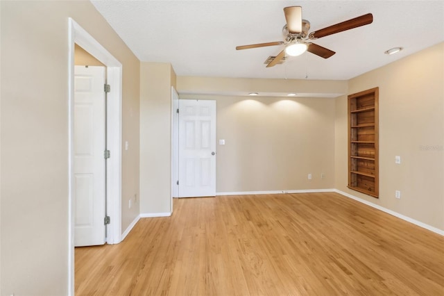 empty room with built in features, light wood-style floors, baseboards, and a ceiling fan