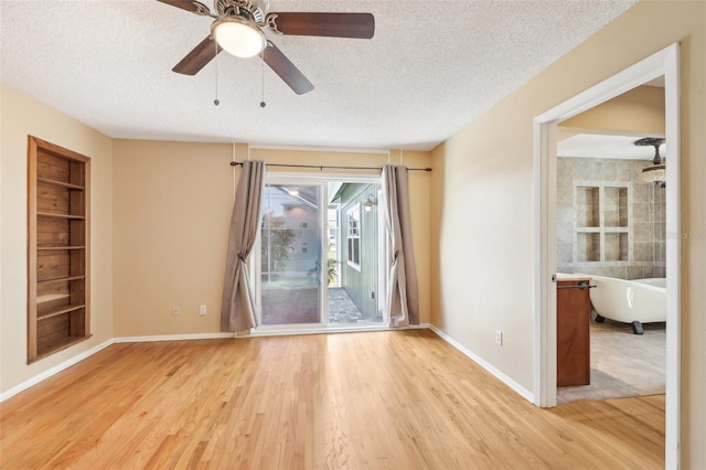 empty room with built in shelves, light wood-style flooring, a textured ceiling, and baseboards