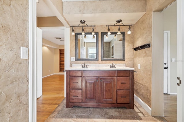 full bath featuring a sink, double vanity, baseboards, and wood finished floors