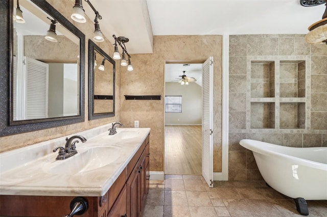 full bath with double vanity, a soaking tub, a sink, and tile walls