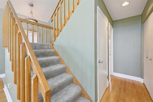 stairs featuring a textured ceiling, baseboards, and wood finished floors