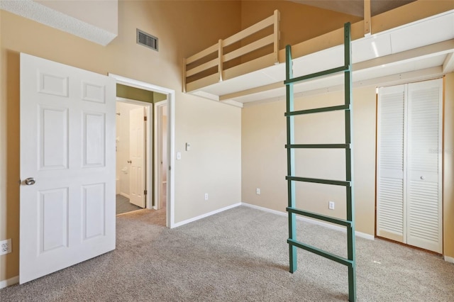 unfurnished bedroom featuring baseboards, visible vents, a towering ceiling, carpet flooring, and a closet