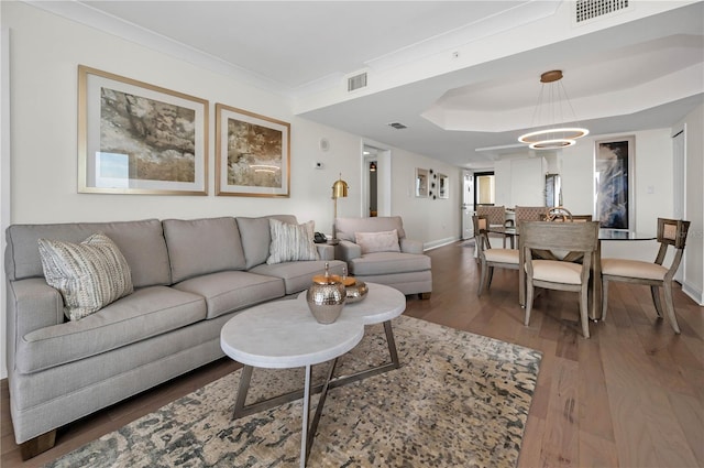 living room featuring ornamental molding, visible vents, baseboards, and wood finished floors