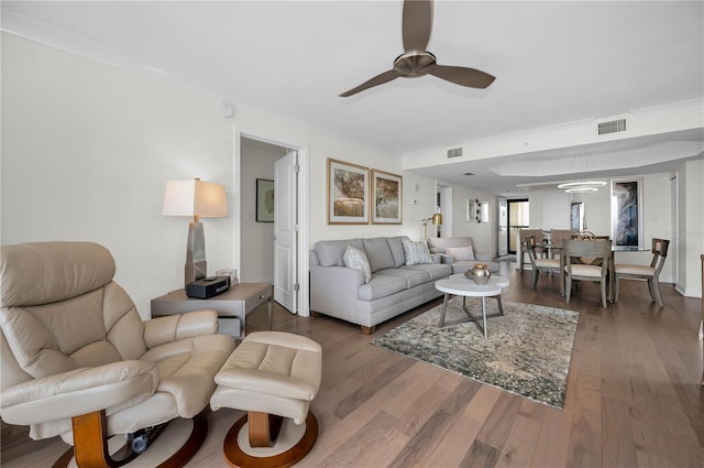 living area with crown molding, visible vents, and wood finished floors