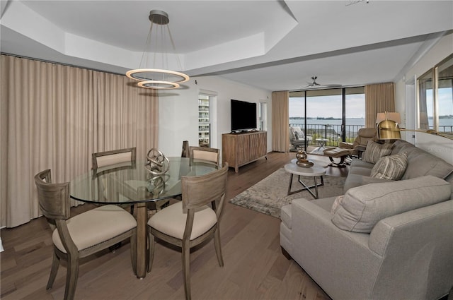 dining room with ceiling fan with notable chandelier, a tray ceiling, floor to ceiling windows, and wood finished floors