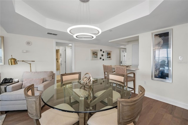 dining space with wood finished floors, a raised ceiling, visible vents, and baseboards