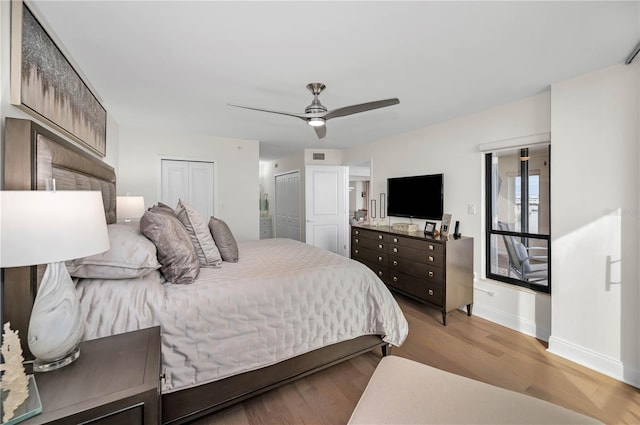 bedroom featuring a ceiling fan, baseboards, wood finished floors, and two closets