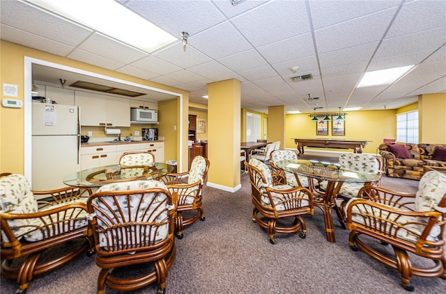 dining area with a paneled ceiling, dark carpet, visible vents, and baseboards