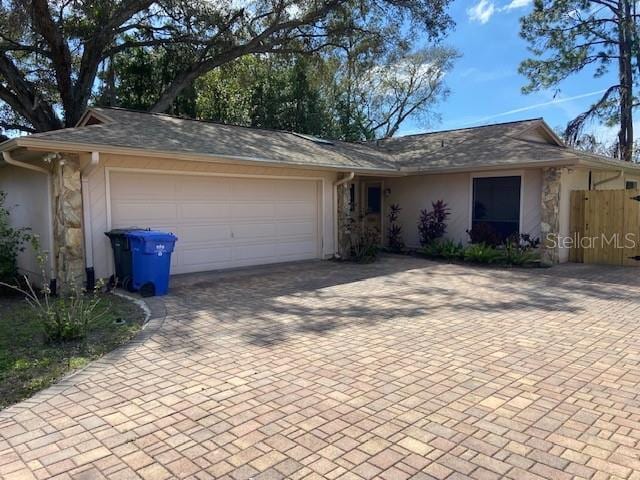 ranch-style house featuring decorative driveway, fence, an attached garage, and stucco siding