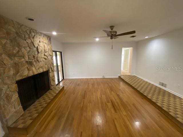 unfurnished living room with visible vents, a ceiling fan, a stone fireplace, wood finished floors, and baseboards