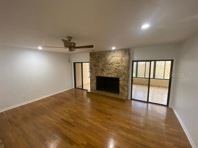 unfurnished living room featuring a stone fireplace, recessed lighting, wood finished floors, and baseboards