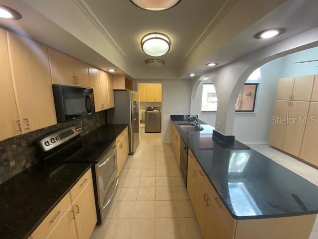 kitchen with arched walkways, light tile patterned floors, stainless steel appliances, a raised ceiling, and a sink